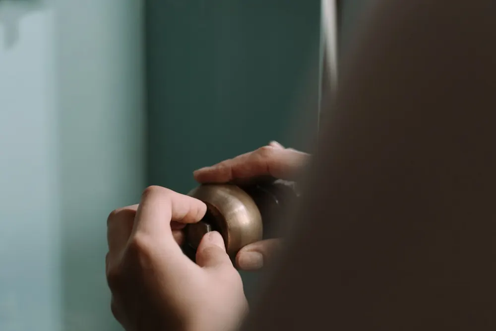 Hands loosening a brass fitting on a pipe against a pale wall