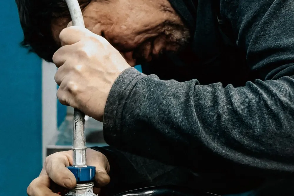 A technician bent over a water pump, fitting a hose