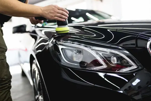 A polishing pad on black paint above a headlight, with studio lights reflected