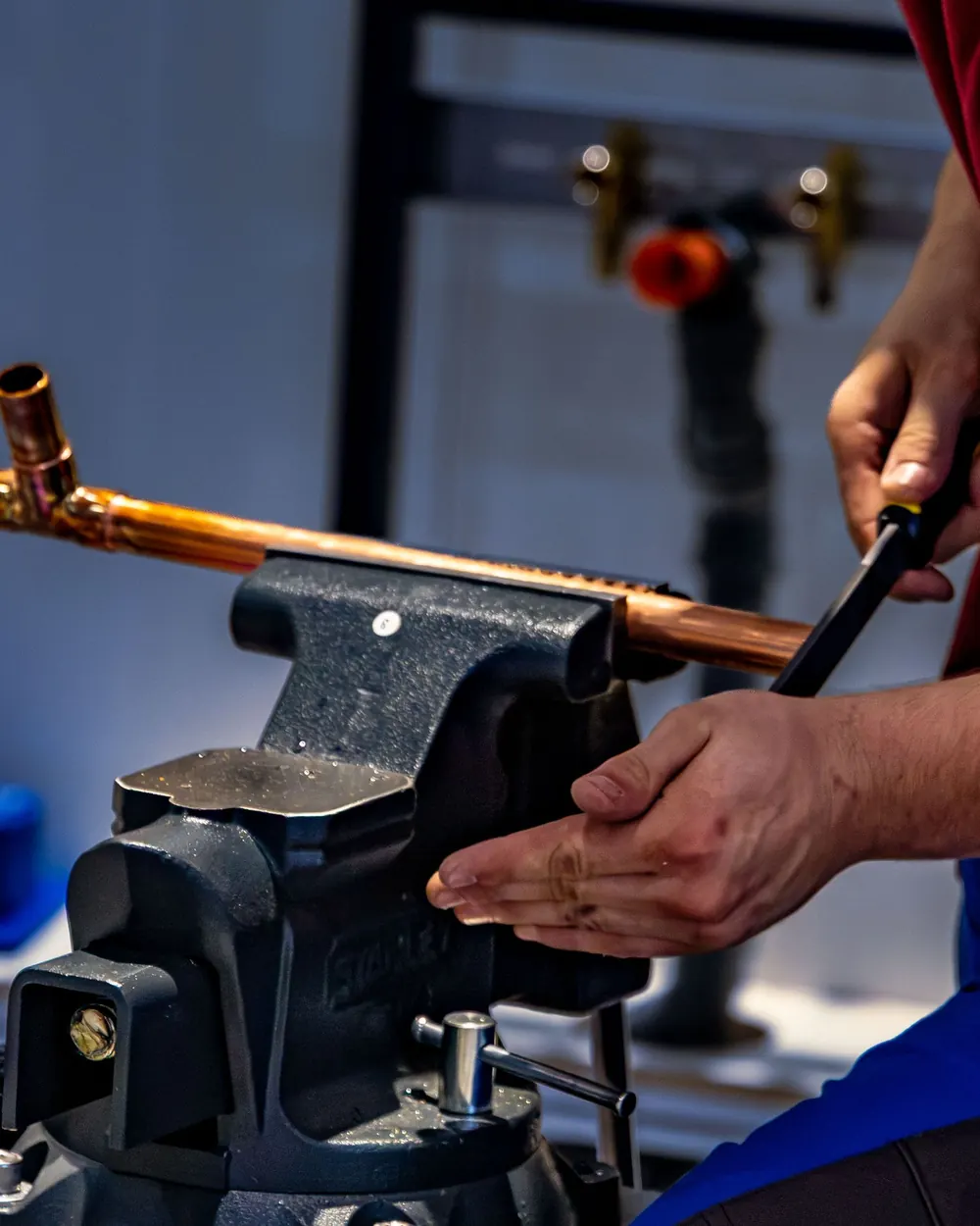 Hands tightening a length of copper pipe in a bench vise