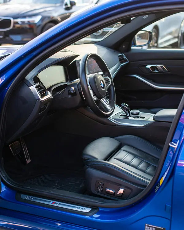 A clean black leather driver's seat and dashboard seen through an open door