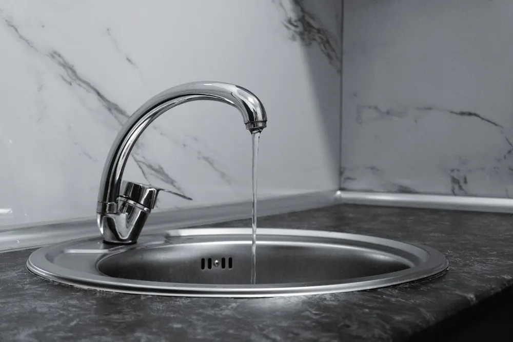 A chrome kitchen faucet running into a round steel sink
