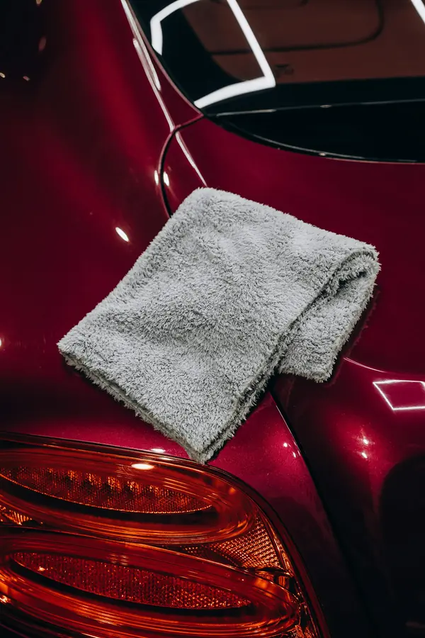 A folded grey microfibre towel on glossy red paint above a tail light