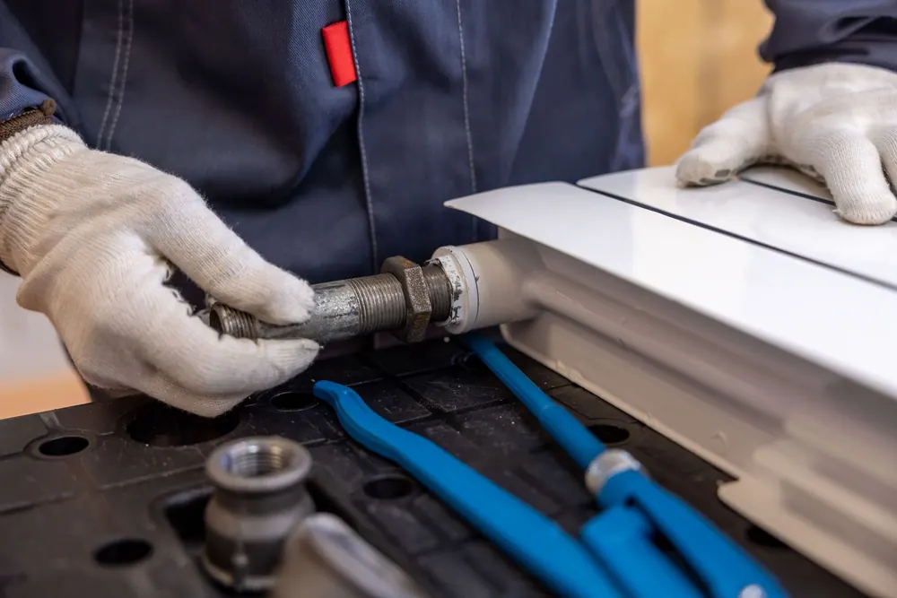 Gloved hands threading a metal fitting onto a pipe, with blue tools on the bench