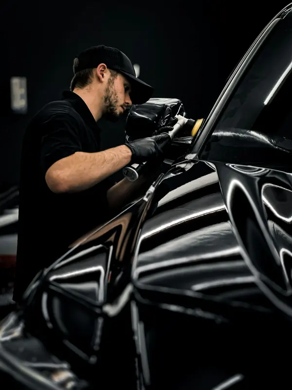 A detailer polishing the wing mirror of a gloss black car